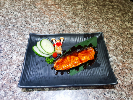 Grilled salmon with vegetables served on black stone plate on wooden tableの写真素材
