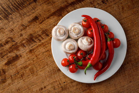 Mushrooms, red pepper, cherry tomatoes on a white plate on a wooden backgroundの写真素材