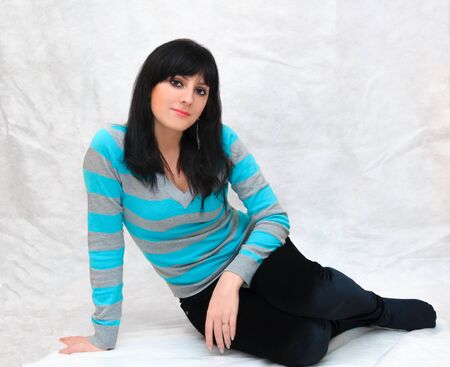 Portrait of a young beautiful woman, smooth healthy skin with minimal makeup, naturalness and beauty. Charming brunette on a gray background, sitting on the floor.の写真素材