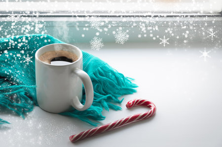 A mug of hot coffee is on the windowsill. Nearby lies a blue scarf and candy cane.の写真素材