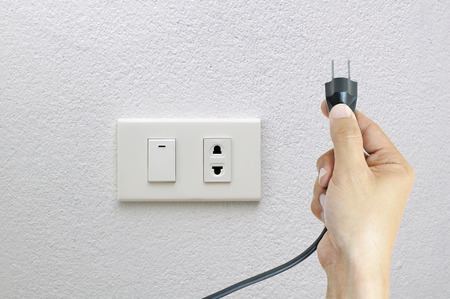Hand putting plug or unplug on socket and white wall backgroundの写真素材