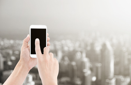 Hand holding white smart phone and touch on black screen on city landscape backgroundの写真素材