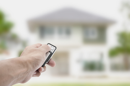 Hand of man holding remote with house blur background , security safety concept businessの写真素材