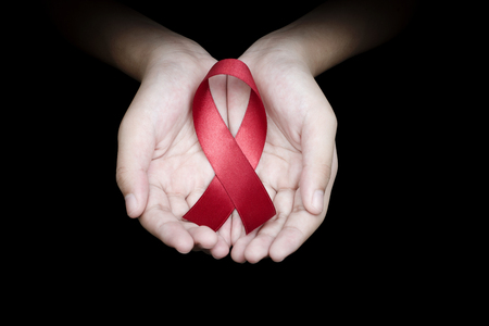 Hand holding red ribbon on black background sign of world aids day hiv , 1 december symbol of health cancer dayの写真素材