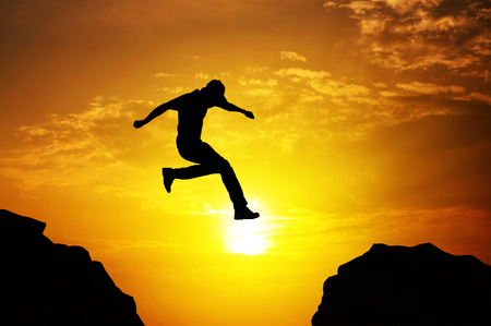 Man jumping over precipice on sunset backgroundの写真素材