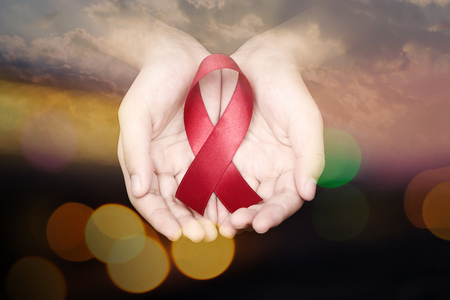 Hand of women holding red ribbon on dark sky and bokeh background sign of world aids day hiv , 1 december symbol of health cancer dayの写真素材