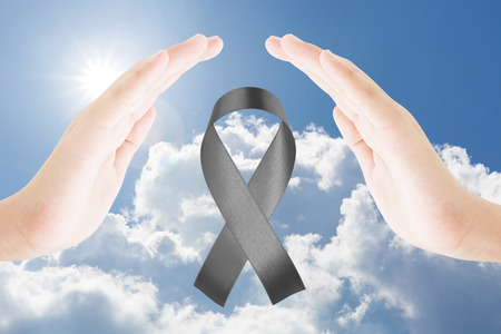 Two hands female protect awareness black ribbon on blue sky clouds and sun backgroundの写真素材