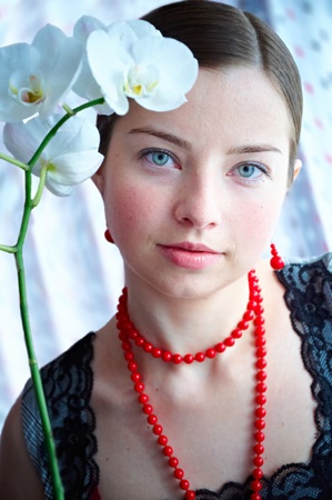 The beautiful girl in a red beads with an orchidの写真素材