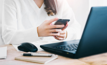 Close up of hand young female using mobile phone to searching information while she working with...