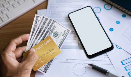 Close-up of hand  businessman holding credit card and dollar with mobile phone and paperwork on deskの写真素材