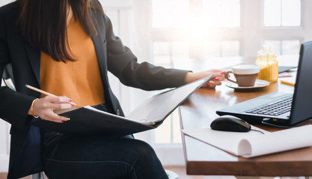 Young asian woman wearing casual suit with jean. she reading document while  working and drink...