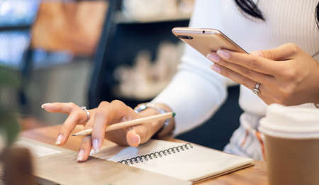 Close-up of hand business woman using mobile phone to searching information from internet while she working with laptop on deskの写真素材