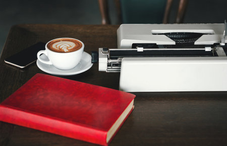 Place of work on desk have old typewriter, red book, mobile and coffee. Concept working with retro equipment and modern deviceの写真素材