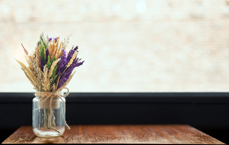 Colorful of dry flowers in glass bottles on old wooden table with bright background