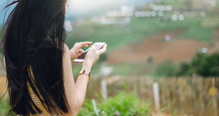 Young asian woman standing on the hill and  using smartphone working and connect people. Concept online system can be used anywhereの写真素材