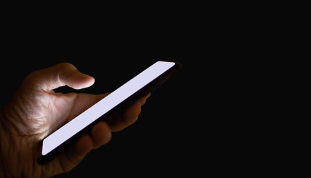Close-up of hand holding mobile phone on dark background. Concept hacker using mobile phone to steal...