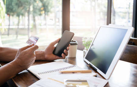 Young man using credit card with smart phone and digital tablet on deskの写真素材