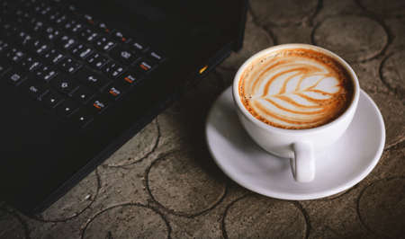 Closeup latte art coffee in white cup and laptop on table made of stone with Circle patternの写真素材