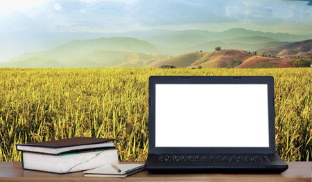 Laptop and books on desk with rice field and mountain backgroundの写真素材