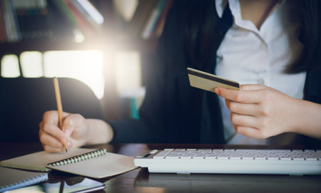 close-up businesswoman holding credit card and writing information on notebook