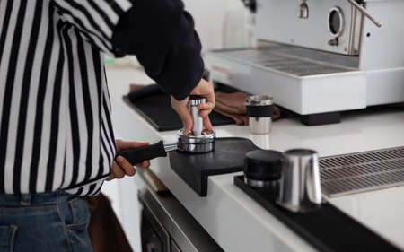 Close-up, barista holding tamper going to press ground coffee in holder to make coffee in white tone cafeの写真素材