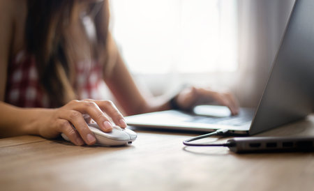 Focus on hand young asian woman holding computer mouse and using laptop working at home