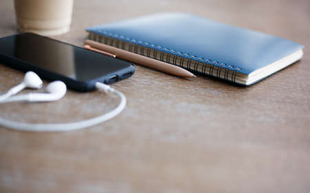 Focus at pen and blue notebook on wooden table with mobile,  headphone and coffeeの写真素材