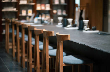 Selective focus in front of wooden seat with coffee counter and blur coffee making equipment background. design for cafe or homeの写真素材