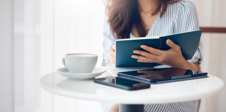 Asian businesswoman reading an appointment in note book during a break with coffee drink, on white...