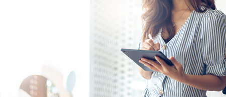 Focus on hand young asian businesswoman standing and using stylus pen writing on computer tablet to...