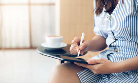 Young asian woman in casual clothes using modern digital tablet working online at cafe during a break with coffee drinkの写真素材