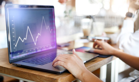 Young asian business woman sitting at table in cafe and working with stock trading on laptop...