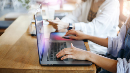 Young asian business woman sitting at table and using computer laptop working with friend in cafe,...