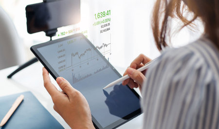 Young asian businesswoman using tablet computer with digital screen of investment chart working with...