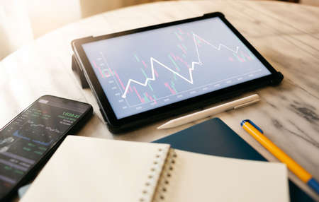 Desk office with digital tablet, mobile phone and notebook, Close up view and select focus on screen with chart of investment , Concept of financial analysisの写真素材