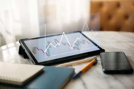 Desk office with digital tablet, mobile phone and notebook, Close up view and select focus on screen with double exposure of investment chart, Concept of financial analysisの写真素材