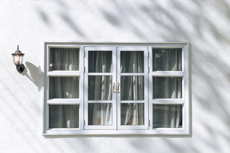 White window frame on white concrete wall with curtain inside and lamp hanging on the left with...