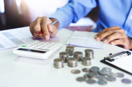 Asian businessman on desk in office using calculator to calculate saving account passbook and statement with financial report. concept of saving for the future and family , close-up viewの写真素材