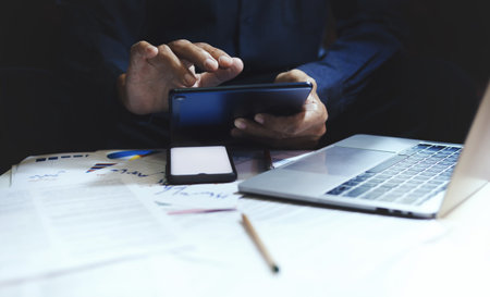 Close-up view, hand of businessman using tablet searching data online working on laptop and meeting with business group to make marketing and investment plan for the futureの写真素材