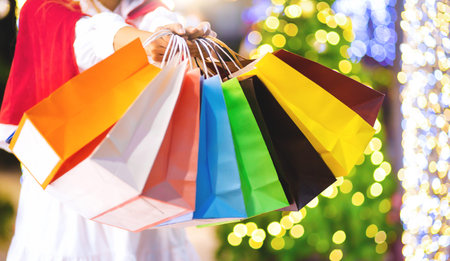 Female hand holding many colorful shopping bags on bokeh backgroundの写真素材