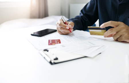 Asian businessman hand holding credit card checking invoice and bank statement trying to find money to pay credit card debt and all loan bills. Financial problem from inflation economy conceptの写真素材
