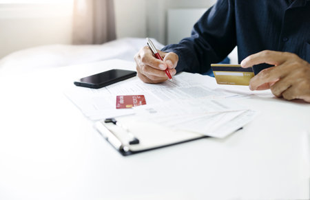 Asian businessman hand holding credit card checking invoice and bank statement trying to find money to pay credit card debt and all loan bills. Financial problem from inflation economy conceptの素材 [FY310201211097]