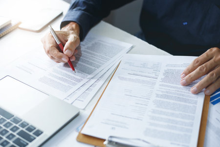 Asian businessman reviewing document reports at office workplace with computer laptop. legal expert, professional lawyer reading and checking financial documents or insurance contractの写真素材