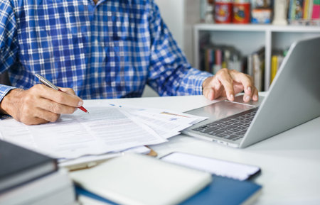 Businessman holding pen checking financial report or business contract from documents to make new...