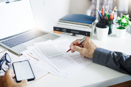 Businessman investor checking financial reports or business contract from documents lying on his desk, A man working or meeting online with computer laptop on desk at homeの写真素材