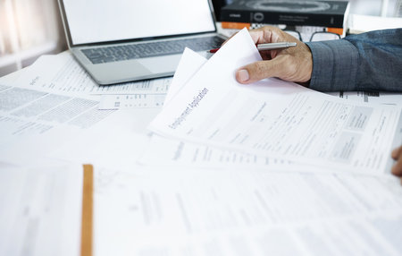 A man reading employment application form and many information in documents on desk. he using laptop to find a new job after losing his job during the recessionの写真素材