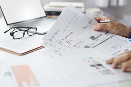 A man working at home with computer laptop to start new business online checking order, receipt and inspecting products in catalog before sending to customers onlineの写真素材