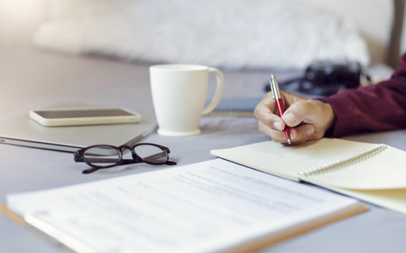 Asian man wake up in the morning holding pen writing note and working with document on bed with...