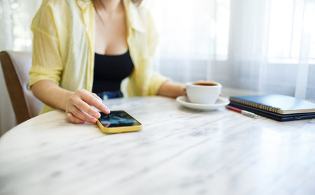 Young Asian woman in casual clothes sitting in cafe with coffee drink using mobile phone for...
