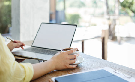 Close-up shot, young asian woman in casual clothes holding coffee cup while working with laptop at...